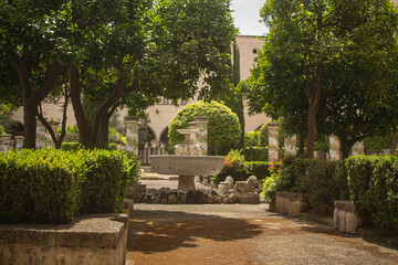 Fototapeta premium Pathway through a park with fountain and beautiful tiled pillars plated at the cloister garden of Santa Chiara Monastery, Naples, Italy. Vacation in Italy