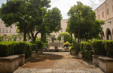 Pathway through a park with fountain and beautiful tiled pillars plated at the cloister garden of Santa Chiara Monastery, Naples, Italy. Vacation in Italy