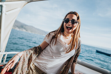 A happy girl with sunglasses is laughing joyfully on a boat with a sea backdrop, embodying a...