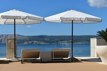 Summer vacation, sun and sea, sunbeds and umbrellas with a view of the blue sea and the landscape.