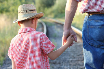 hands of parent and son in cowboy hat near the railroad