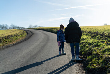 Beautiful winter photo of two little warmly dressed girls with a shadow on a rural asphalt road...