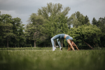 A woman practicing yoga outdoors performs a bridge pose in a peaceful park, surrounded by lush...