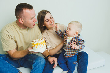 A young family with a baby in their arms sits with a cake in their hands. A married couple is...