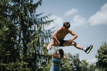 Athletic man performing a mid-air jump over his female friend during an outdoor workout session on...