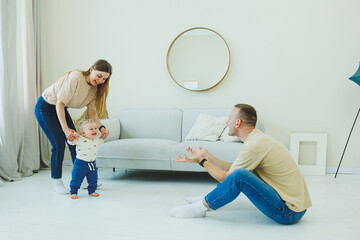 A young married couple is having fun playing with a small child in a modern living room together....