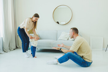 A young married couple is having fun playing with a small child in a modern living room together....