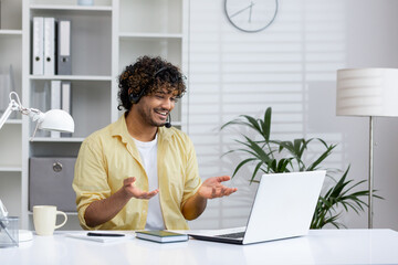 Happy man wearing headphones and smiling while having a video call on his laptop at home in a...