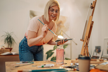 Smiling artistic hipster girl mixing colors on palette at atelier.