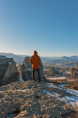 A man stands on top of a rocky mountains and enjoys the beautiful view of Meteora Monastery in...