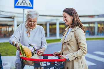 A Caucasian woman gently aids her smiling senior mother as they place shopping bags into the car...