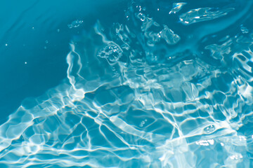 Blue water with ripples on the surface. Defocus blurred transparent blue colored clear calm water surface texture with splashes and bubbles. Water waves with shining pattern texture background.