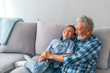 Happy grandfather sit on couch enjoy spending time with preschooler grandson at home, loving...