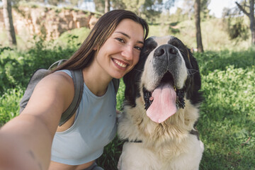 Young woman taking a selfie with her happy dog outdoors. Smiling female hiker and her joyful dog posing for a selfie on a sunny day in nature