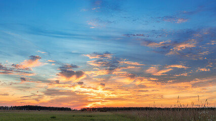 A panoramic view of a vibrant sunset with a vast field in the foreground. The sky is ablaze with orange, pink, and purple hues, creating a stunning display of natural beauty.