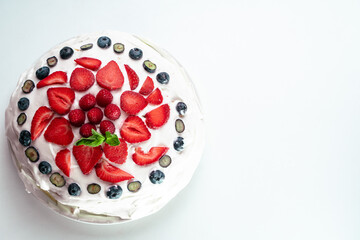Meringue pavlova cake with whipped cream and fresh berries, strawberries, raspberries and blueberries on a white background. Top view, copy space