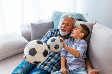 Little boy on couch with grandfather, cheering for a football game and holding a football ball....