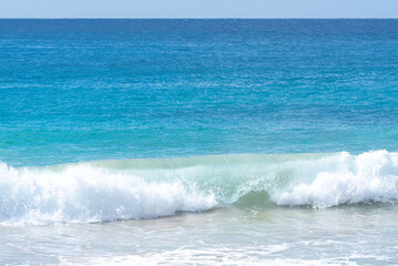 Aqua blue ocean scene with wave breaking on sandy beach