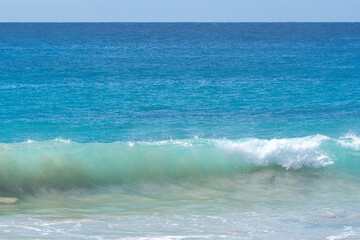 Blue tropical ocean with wave breaking on shore
