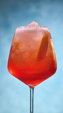 Glass of apperol spritz cocktail with orange slice and straw on blue background. Closeup of summer drink