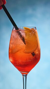 Glass of apperol spritz cocktail with orange slice and straw on blue background. the cocktail straw is placed in the glass, closeup of summer drink
