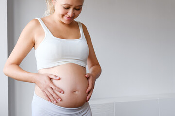 Pregnant Woman Dressed In A Sporty Outfit Holding Her Belly . Expecting Child. Home Indoor...