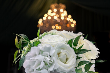White roses in a bouquet in front of a chandelier in soft focus with a black background. 