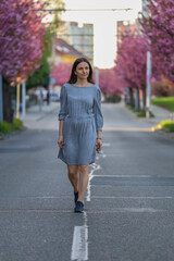 Beautiful girl walks along the street with cherry blossoms