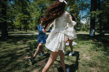 Happy, joyful sisters enjoy a playful dance in a circle on a bright sunny day in the park,...