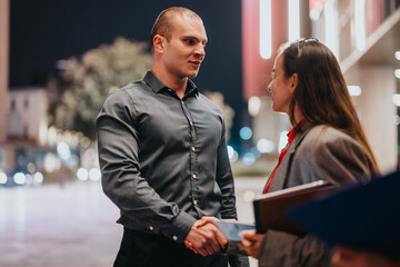 Young corporate business partners shake hands outdoors at night, symbolizing partnership, professionalism, and connection.