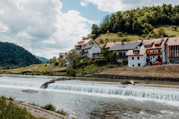 Dam spans a mountain stream, with houses in the distance