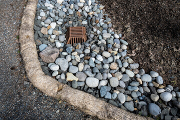 New installation of storm water flood management, iron grate storm drain surrounded by river rock with a Straw Wattle below to prevent debris from reaching the sidewalk or street
