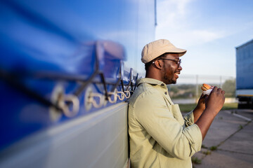 Truck driver enjoying cheeseburger on parking lot.