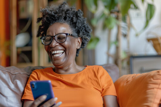 Portrait of a happy senior African American woman sitting on a sofa at home using a mobile phone and laughing,