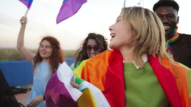 Close up portrait of a group of LGBT poeple having fun celebrating the gay pride day with a rainbow flag. Young adult LGTB friends on a sexual rights party smiling with freedom and courage expression