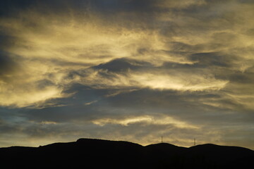 A golden sunset with wispy clouds over a hill horizon
