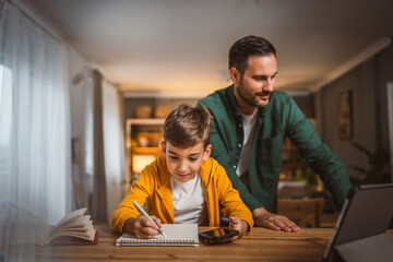 Son copy notes from mobile phone at home with dad at background