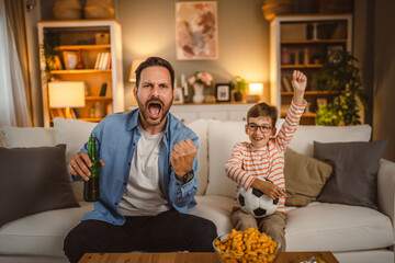 Father and son with football ball watch football match cheer at home