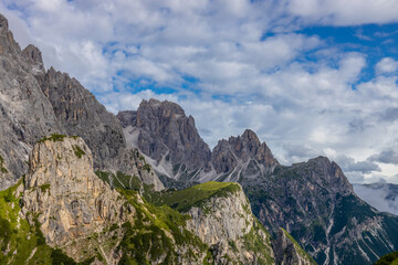 Dolomiti Alps beautiful mountain landscape. Rocky tower alpine summits in the Dolomites. Summer mountain scenic view on the hiking trekking path in the green mountain valley and blue sky with clouds