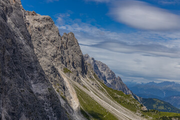 Dolomiti Alps beautiful mountain landscape. Rocky tower alpine summits in the Dolomites. Summer mountain scenic view on the hiking trekking path in the green mountain valley and blue sky with clouds