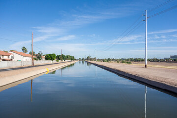 Blue sky with clouds reflecting in calm mirror-like waters bordered by side roads of Arizona canal in a city of Glendale, AZ