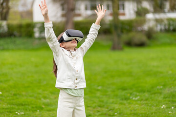 Girl in virtual reality headset with arms outstretched in a park