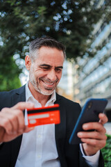Vertical. Mature business man paying with a credit card on a online shopping smartphone...