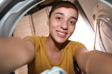 Woman putting clothes into washing machine in bathroom, view from inside. Laundry day