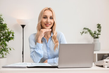 Happy secretary at table with laptop in office