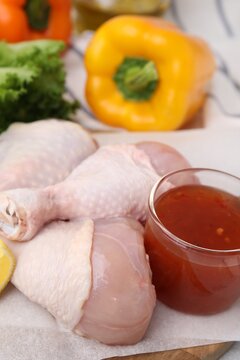 Fresh marinade and raw chicken drumsticks on board, closeup
