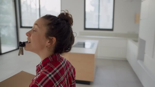 Happy and excited young woman enters her new apartment holding boxes and keys. Moving into new home female is smiling checking out the empty and blank walls. Fresh start visualizing the future