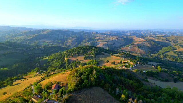 Delightful aerial push-in shot from Penna San Giovanni (MC) with the vivid and sumptuous colors of the typical Marche hillscape in full display, full of thickets, perfectly manicured fields, buildings