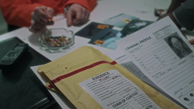 Close-up over-shoulder shot of hands of unrecognizable diverse federal agents looking at criminal profiles, demonstrating photos of dead body to anonymous suspect in handcuffs, smoking cigarette
