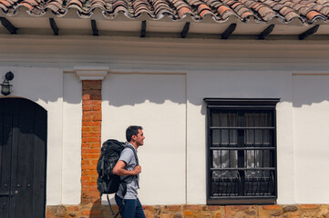 Fototapeta premium young latin man walking with travel backpack in front of a town house